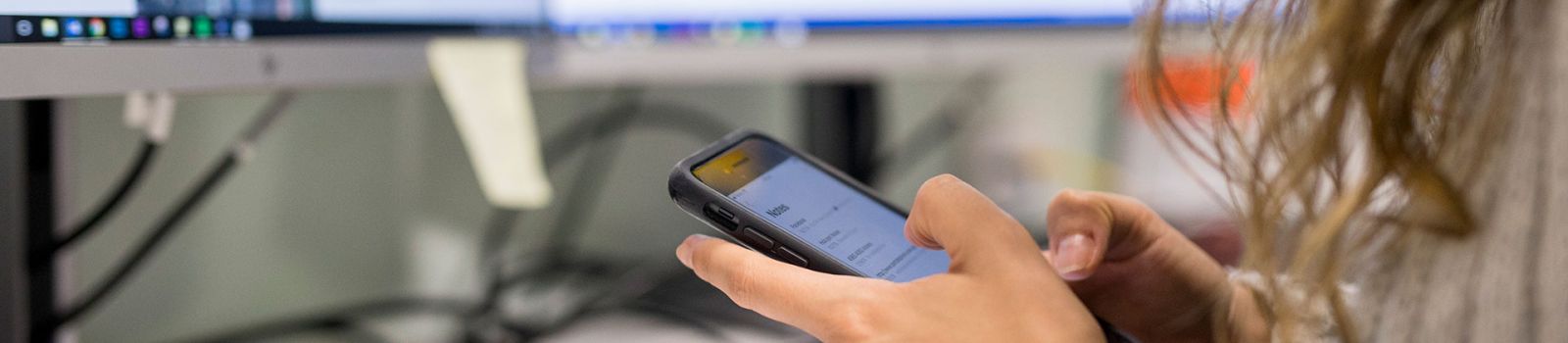 Image of fingers hovering over a phone with a computer in the background  banner image
