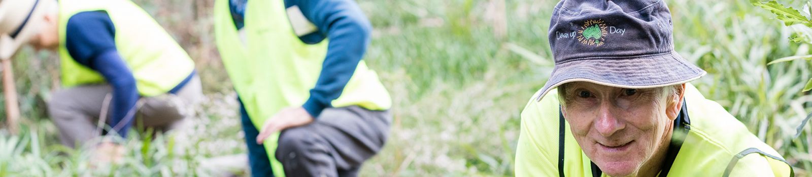 Close up of a man smiling while out in the bush with other people in the distance  banner image