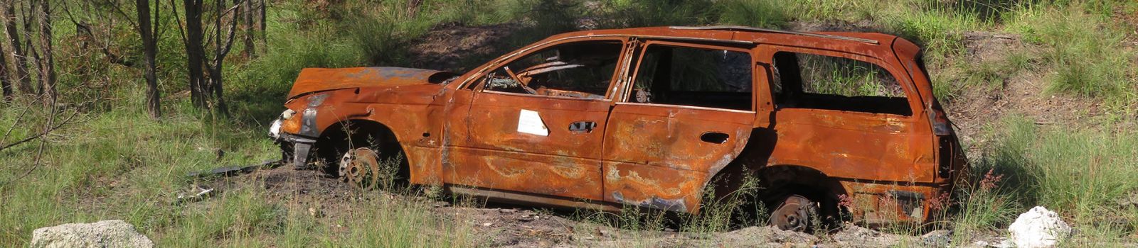 Image of a burnt out car on the side of the road banner image