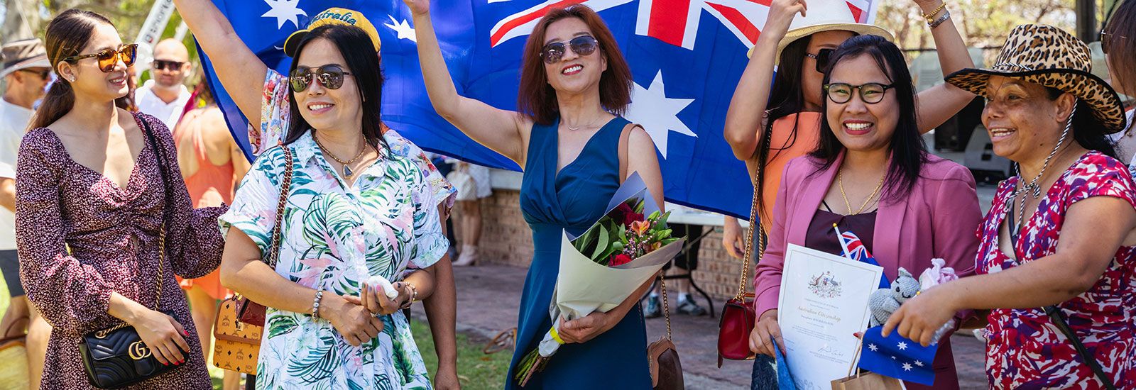 Image of ladies holding an Australian flag to celebrate Australia Day. One lady is holding her Citizenship Certificate banner image