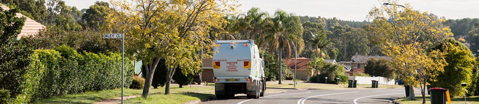 Image of a rubbish truck driving down a road banner image