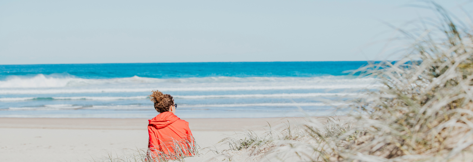 Young female sitting down at the beach banner image