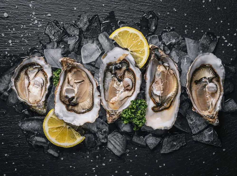 five oysters with lemon and ice on a black plate