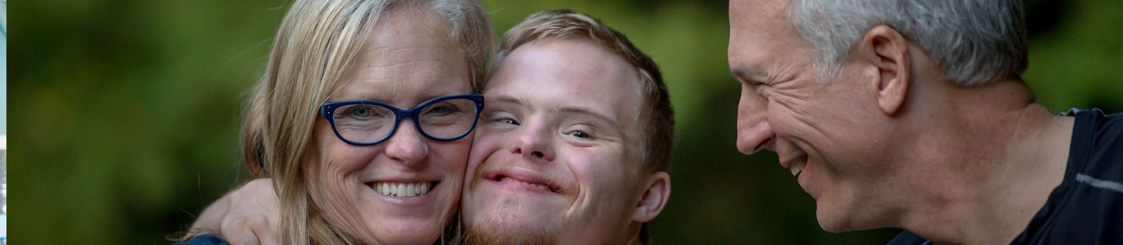 Image of a boy with a disability being hugged by his parents  banner image