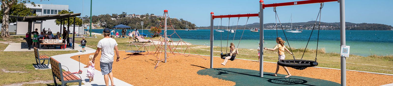 Image of a playground over looking a beach and bay banner image