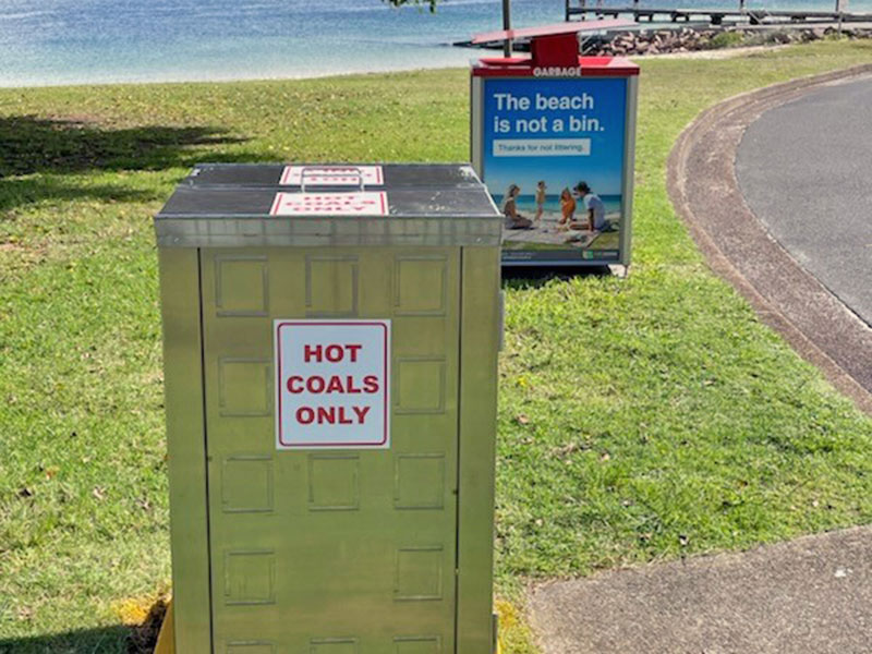 2 bins on grass near the beach. one says hot coals only.