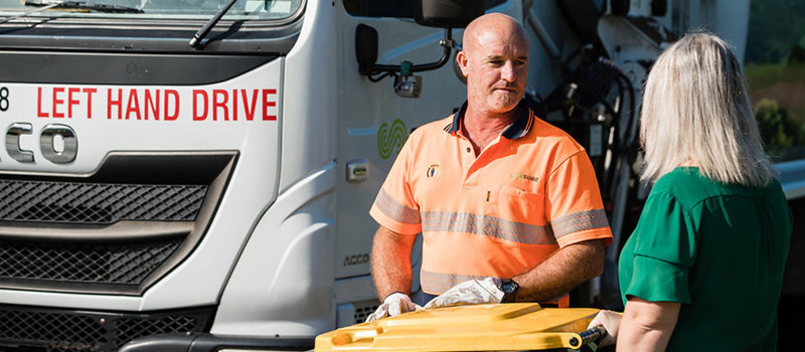 Image of a rubbish truck with a driver and a member of the community  banner image