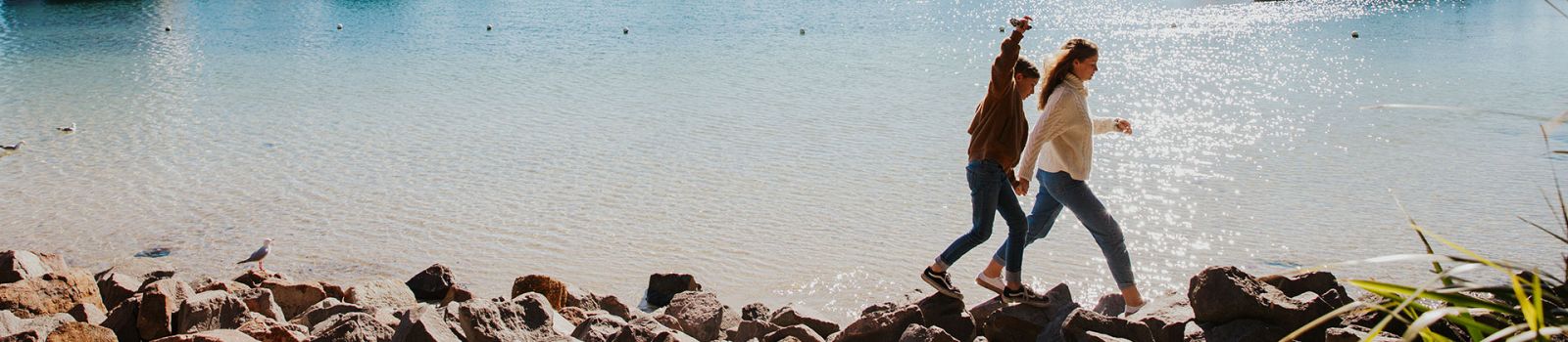 Image of two kids running along a break wall by the beach.  banner image