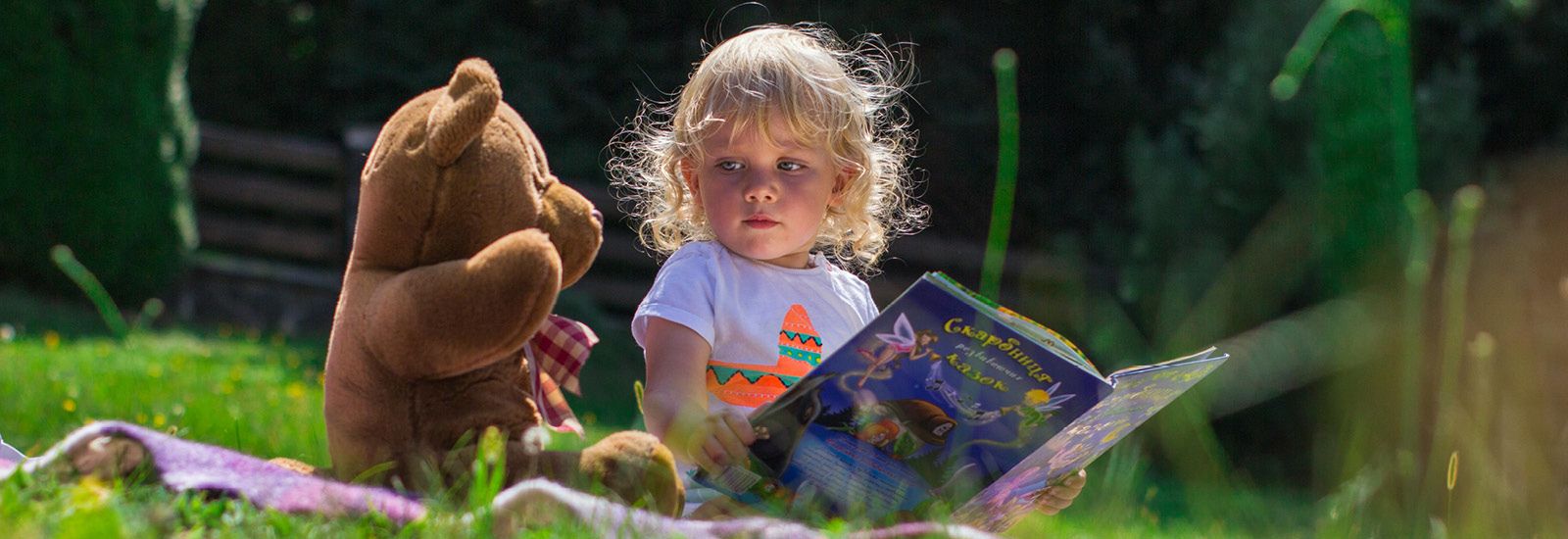 Child reading a book to her teddy bear banner image