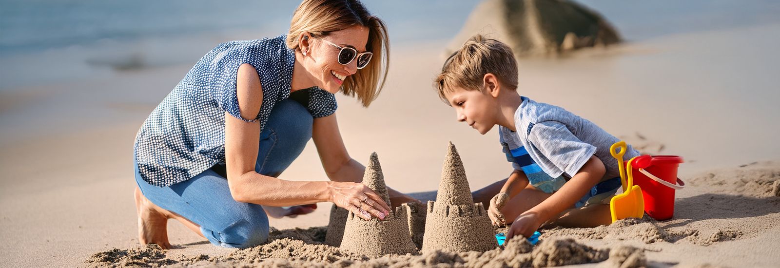 mother and son building sandcastles at the beach banner image
