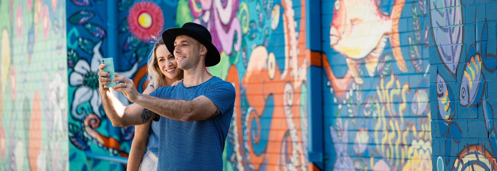 Couple taking selfie in front of street wall art banner image