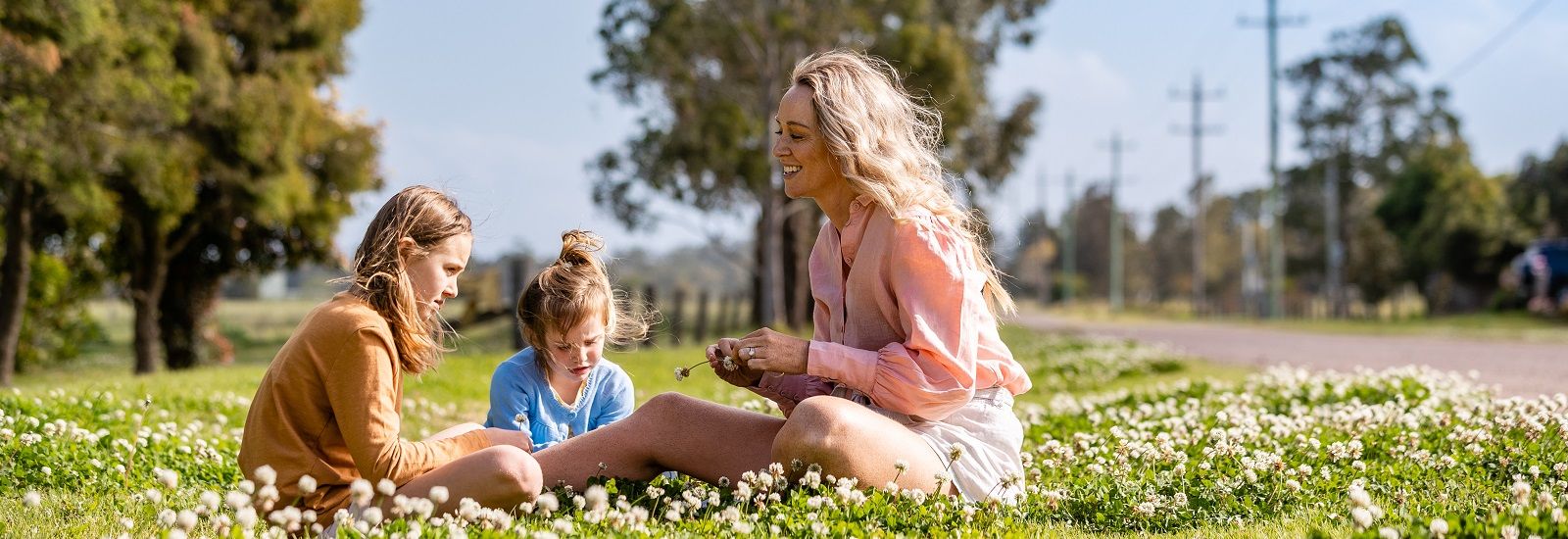 Mum sitting with children on the grass at a park banner image